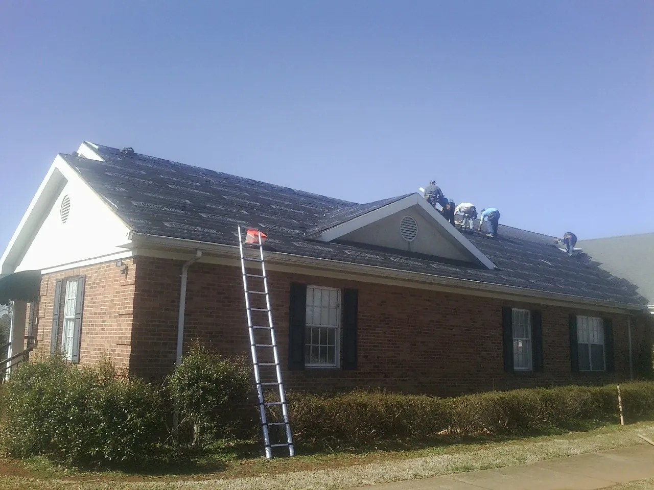 Crew tearing shingles off a brick ranch roof with a ladder set — Metal Roof Repair work by our crew in North Bloomfield