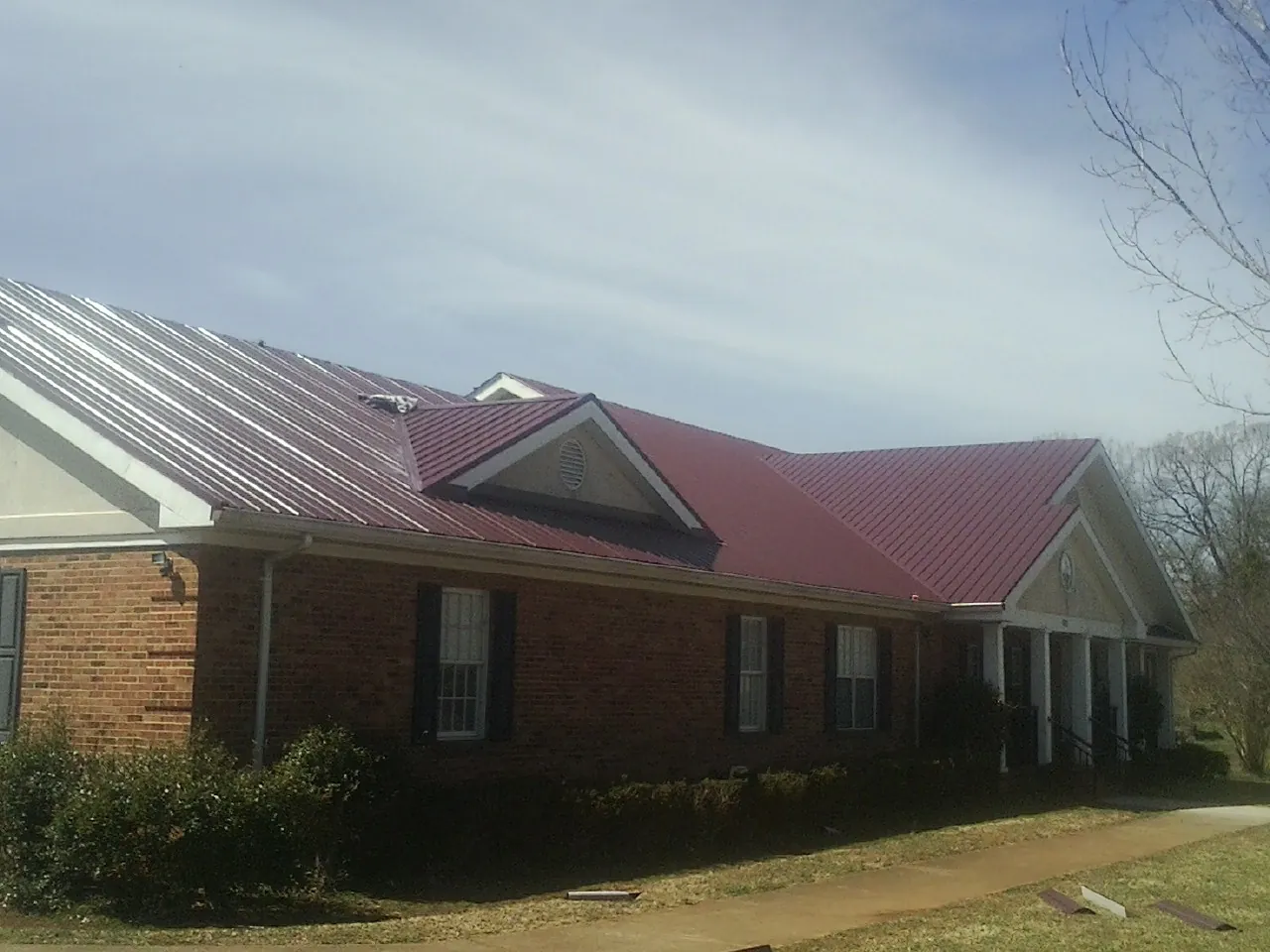 Red metal roof with gabled entries on a long brick building, from a Hail Damage Roof Repair job in North Bloomfield