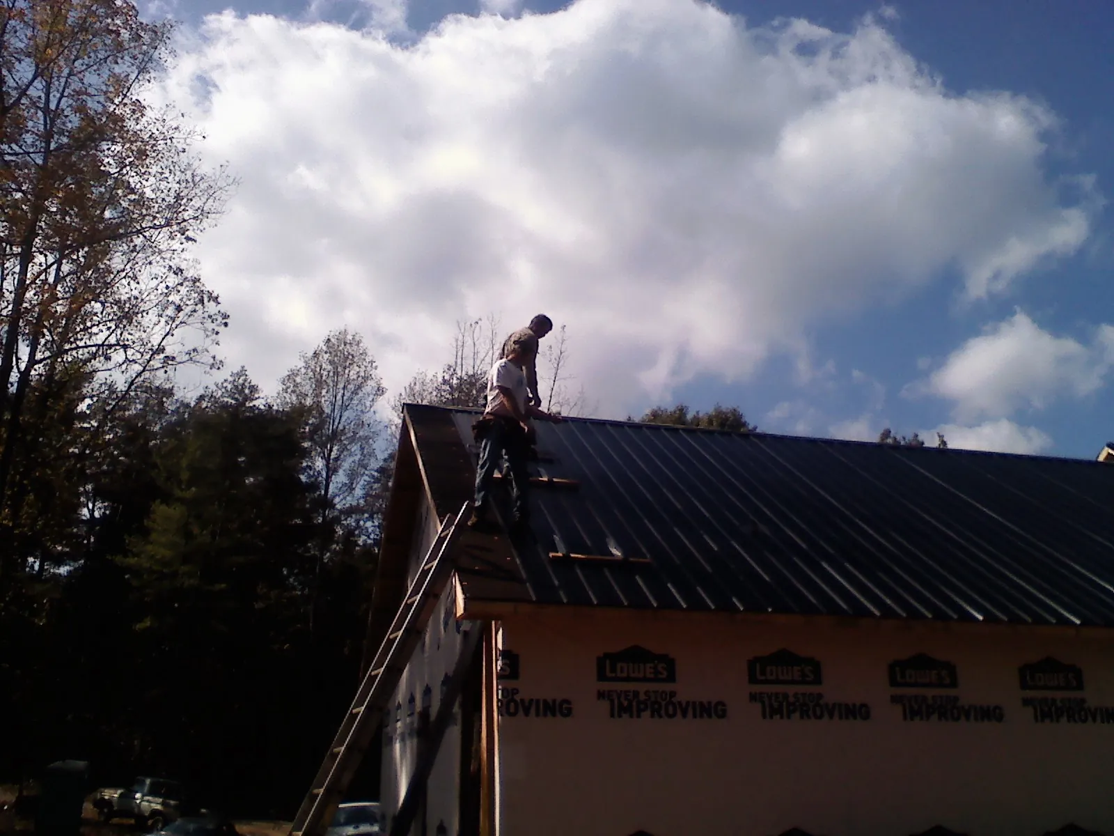 Roofer fastening dark metal panels high against a cloudy sky, from a Roof Inspection job in North Bloomfield