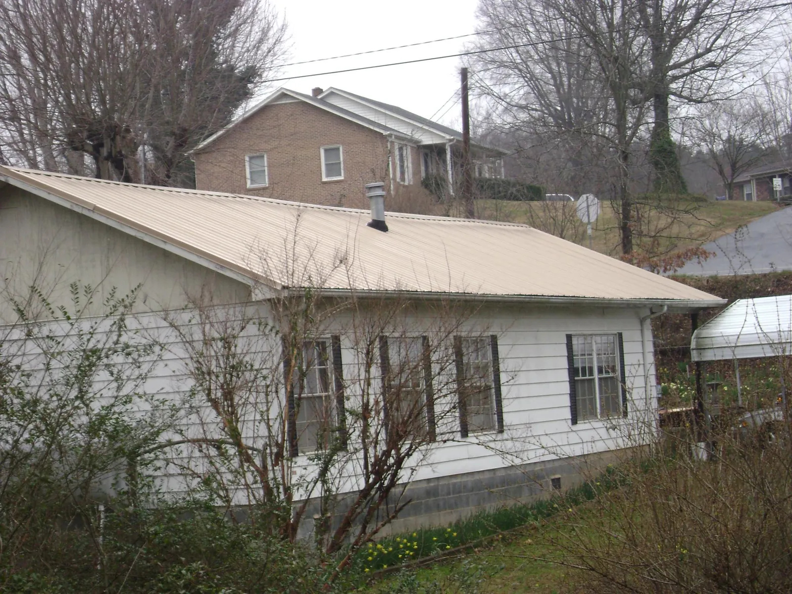 Tan metal roof on a white sided house set into a hillside — Commercial Roofing by Roofing Brothers in North Bloomfield